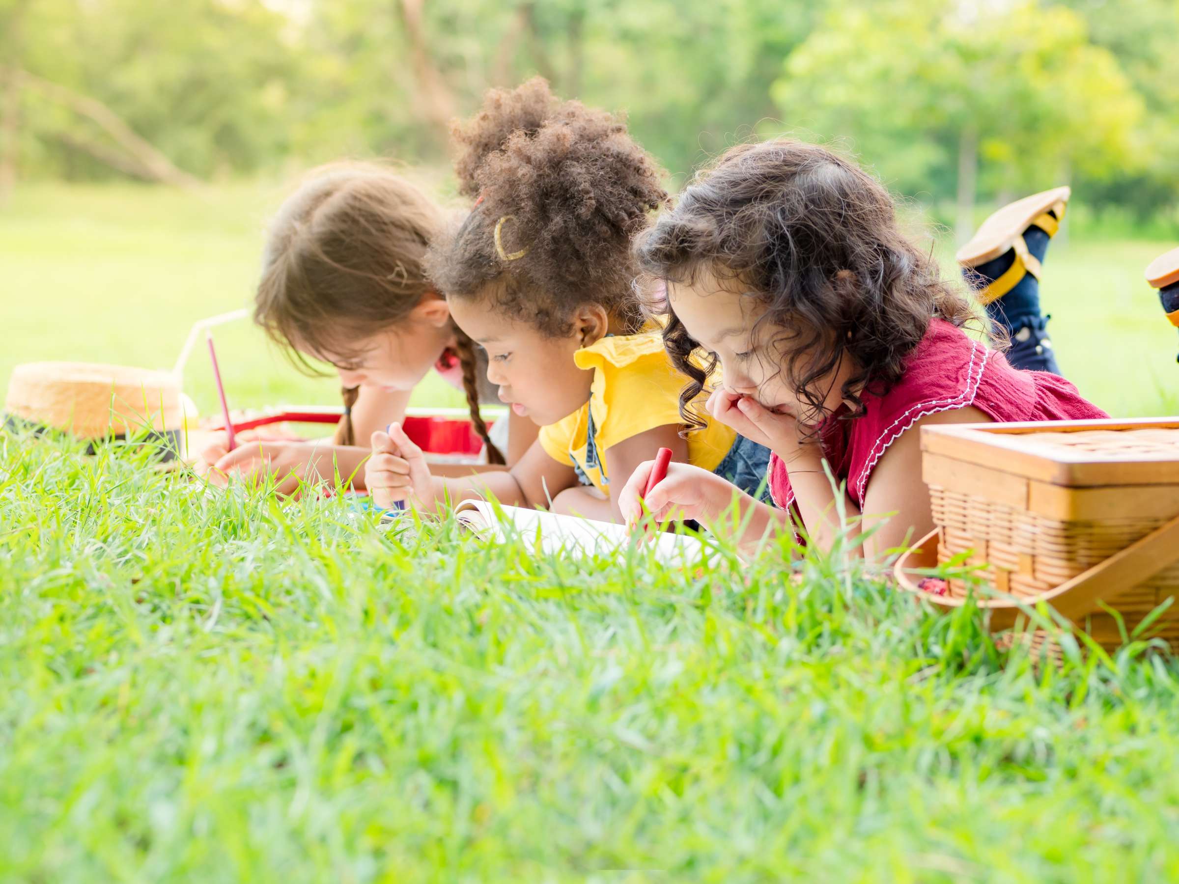 Three children lay on their bellies in the grass, writing in journals.