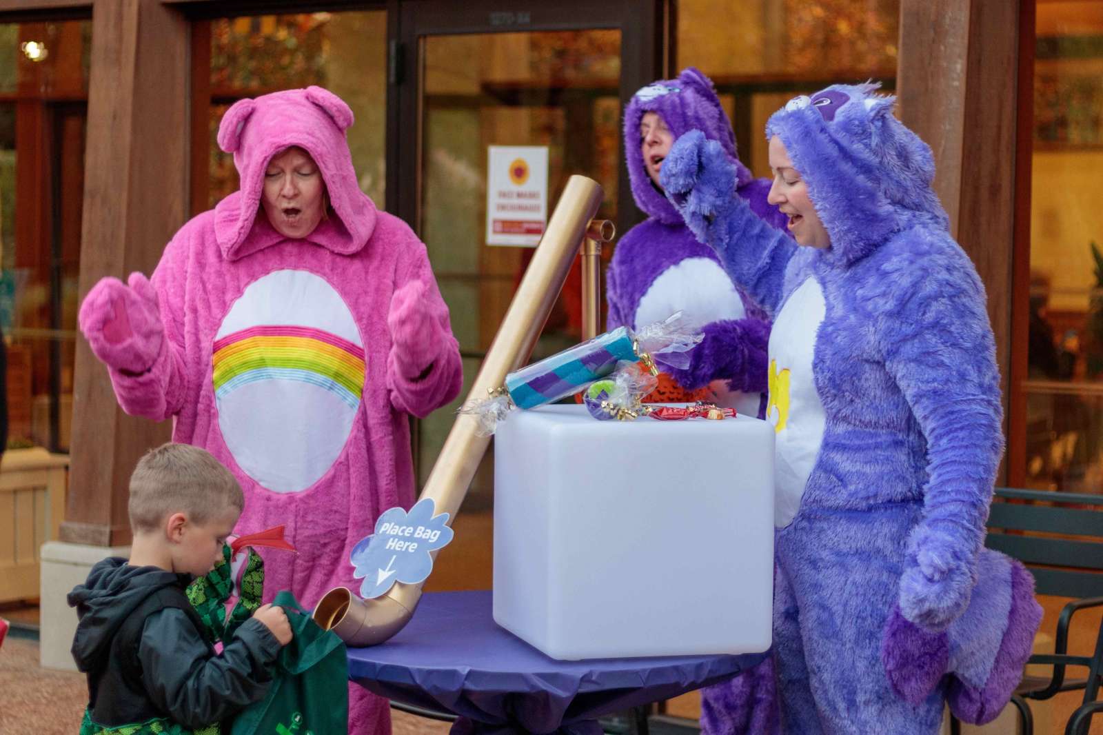 Women dressed as Care Bears give out candy to a child in costume